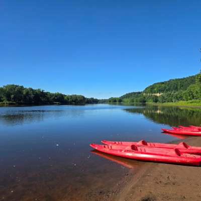 Red kayaks on a calm river shore with trees under a clear blue sky.