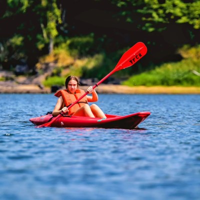 Person kayaking on a calm lake wearing an orange life vest.